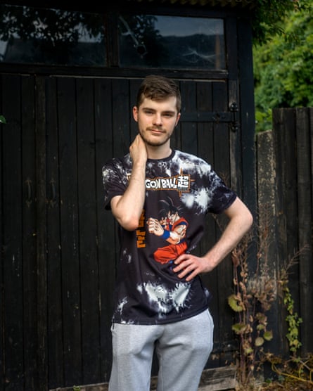 A young man with a shy smile and wearing a Japanese manga T-shirt