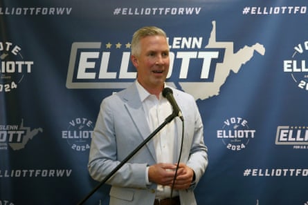 a man in a pale blue blazer with grey hair speaks into a microphone