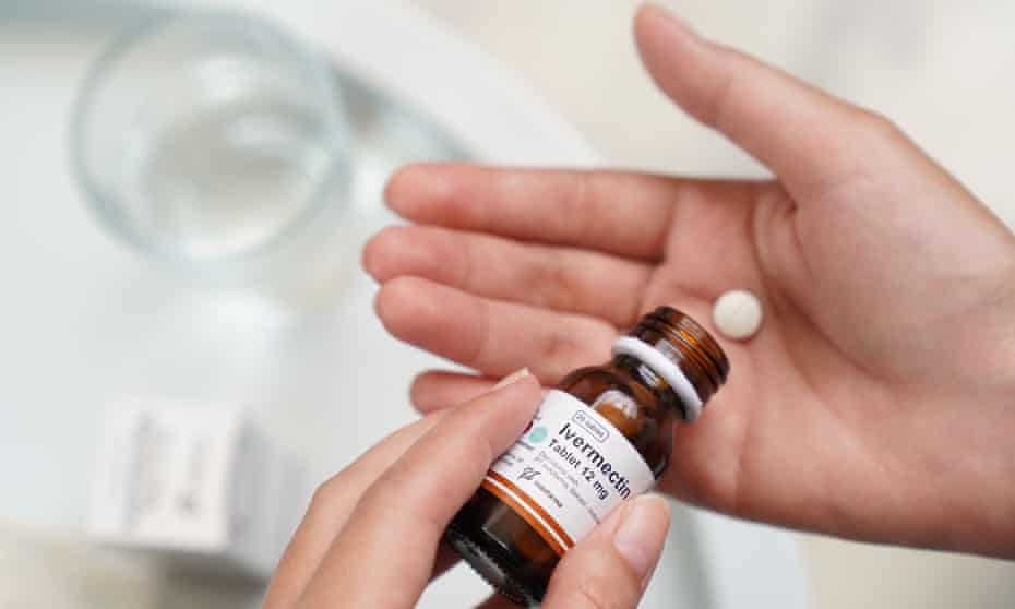 A closeup of a bottle of ivermectin and a hand holding a tablet