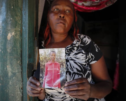 Rose Wanyua Wanjiku leans against a doorframe and holds a picture of a younger Agnes who is wearing a red jumper