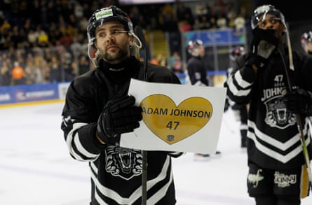 Ollie Betteridge, a British forward for Nottingham Panthers, wearing a neck guard, holds a sign after the match.