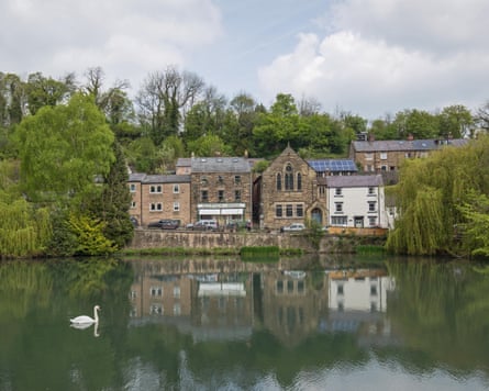 A pond with grey stone houses, a church and trees behind it