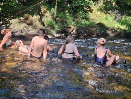 Five people wearing swimming costumes, sitting in a river