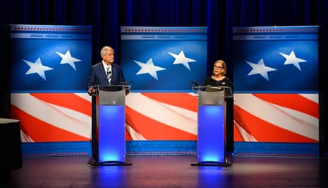 a man and woman stand on stage behind lecterns, an american flag backdrop behind them