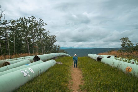 A man in a blueshirt walks among large metal pipes outside