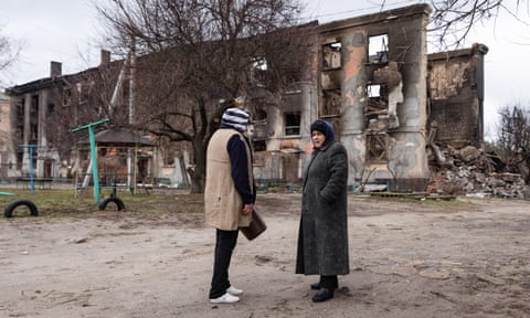 Two women talk in front of a destroyed building in Schastia