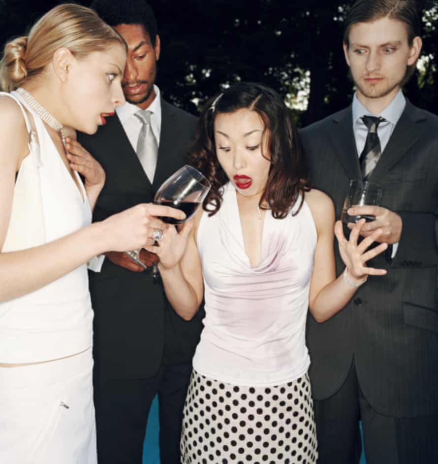 Two women at an outdoor party, one of whom has accidentally spilled wine on the other, with two men in the background.