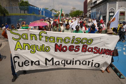 Protesters marching along a city street behind a banner with writing in Spanish
