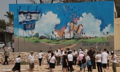 A crowd is gathered in front of a detailed mural on the side of a building showing the police station being blown up.