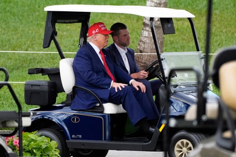 two men in suits ride in a golf cart