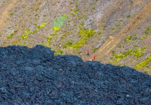 People walk past dried lava at the bottom of a rocky slope