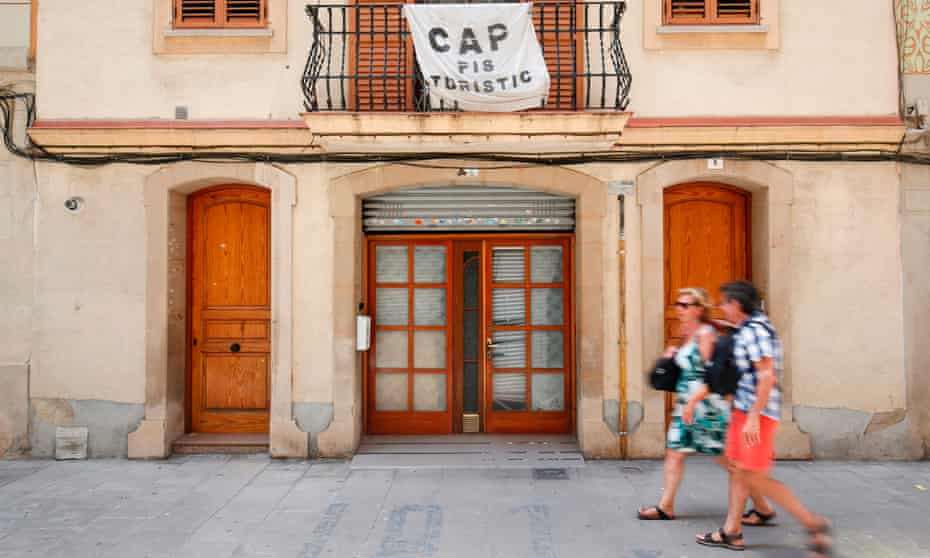A couple passing under a banner reading ‘No tourist flats’ in protest against holiday rental apartments for tourists in the Barceloneta neighbourhood of Barcelona.