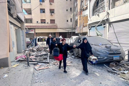 People in Beirut carry bags with them as they walk through a street covered in debris and wreckage