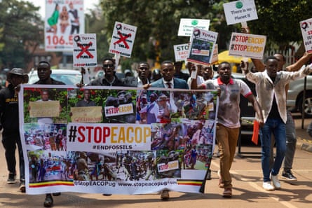 A group of young Africans dressed casually and holding signs above their heads and a banner that says #StopEacop march on what appears to be a sunlit brown road.