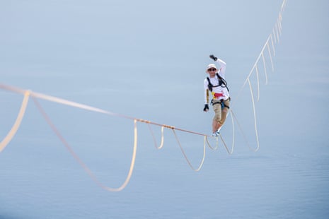 Jaan Roose balances on a highline rope high above the sea, raising his fist and smiling