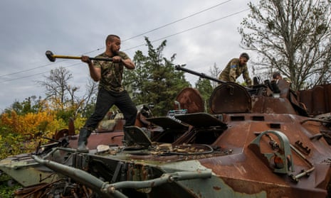 Ukrainian soldier swings a sledge hammer as he stands on top of a rusted military vehicle