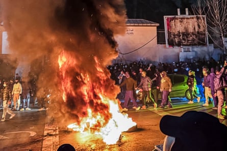 A fire burns on a street in Tehran at night as a group of protesters walk next to it