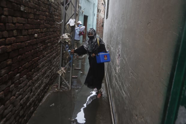A health worker walks through a narrow street full of sewage with a medical kit.