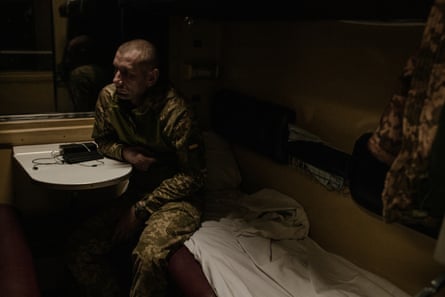 Мъж, облечен във военно облекло, седи на спално легло, облегнат на малка масичка