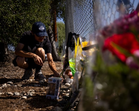 A person adjusts flowers at a memorial near a fence