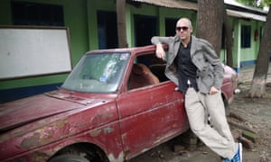 A man leans against an old red car
