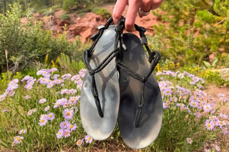a hand holding a pair of sandals in front of wildflowers