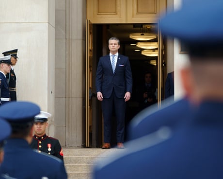 a man in a suit stands at the entrance to a building as men in military uniforms stand by