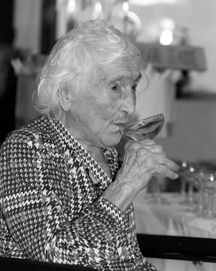 An elderly woman sips wine from a glass in this black and white photograph.