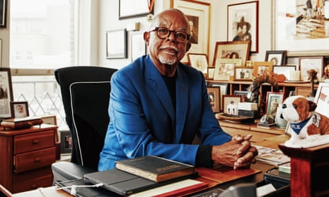 Henry Louis Gates sitting at a desk surrounded by photographs and books.