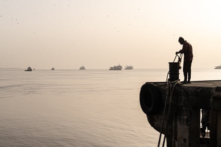 A man holds a rope on a quay. Several boats can be seen on the water in the distance