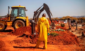 An undertaker wearing personal protective equipment watches as an excavator fills the grave of a Covid-19 victim at the Westpark cemetery in Johannesburg, on 22 July 2020.