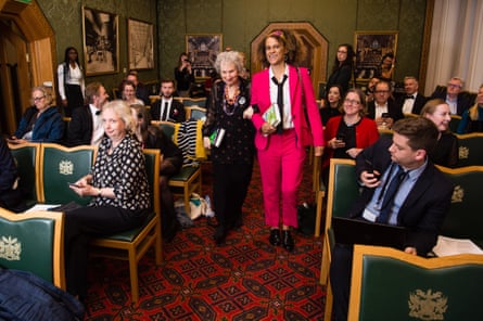 Margaret Atwood and Bernardine Evaristo walk down an aisle between rows of chairs, arms linked, at a Booker prize photocall