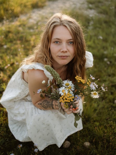 Emma Cardinal crouches in a field holding a bunch of wild flowers