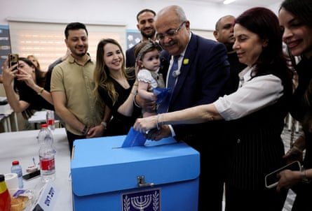 Tibi holding a toddler, putting his ballot in the box