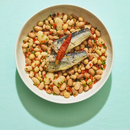 Sardines and beans and red chilli in white bowl against green background