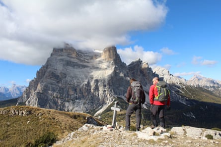 Two people on a mountain summit looking at a cloud-topped peak in the distance.