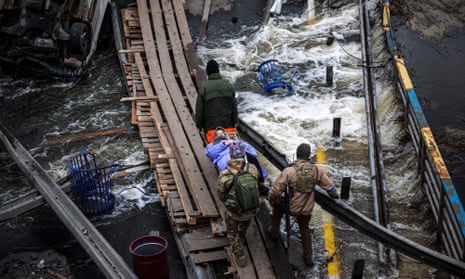 Ukrainian servicemen carry an elderly woman on a stretcher on a makeshift pathway across a river next to a destroyed bridge in Irpin, northwest of Kyiv.