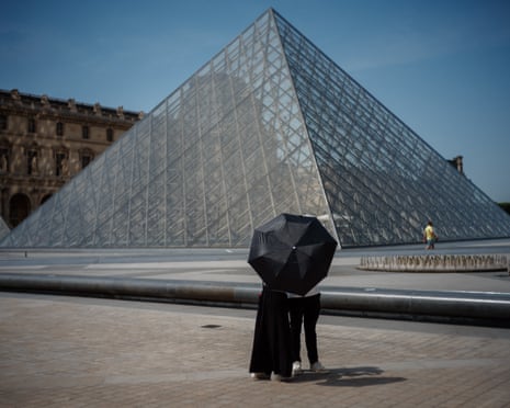 A couple protect themselves from the sun under an umbrella in front of the Louvre Pyramid in Paris, France.