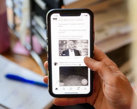A close up of a hand holding a phone displaying a grey tinted social media feed