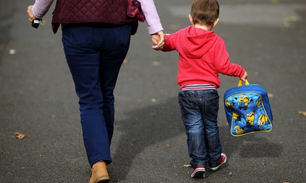 Anonymous shot from behind of woman holding hand of young boy carrying lunchbox