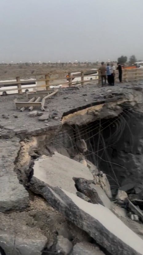People stand on a bridge where it has sustained heavy damage.