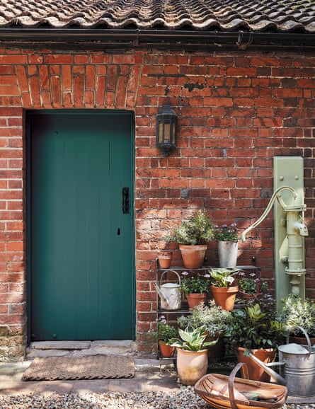 A dark green solid wooden front door in a bare brick country cottage with terracotta pots to one side