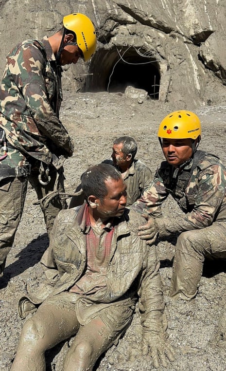 Two army personnel in uniform aiding two survivors in the thick mud outside the tunnel.