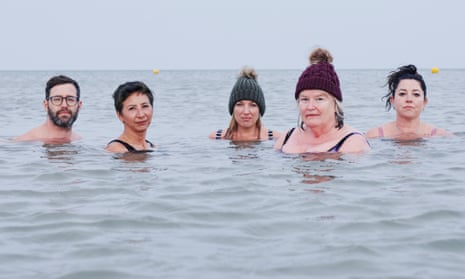 Five people in the sea looking at the camera, three wearing bobble hats