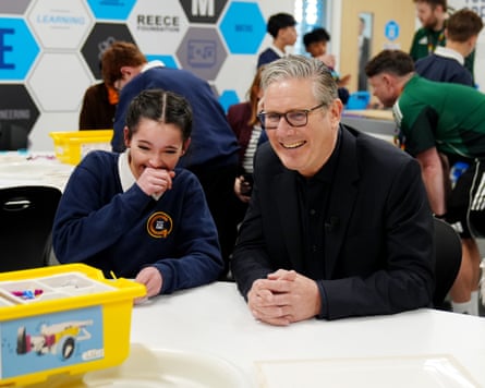 Starmer sits smiling next to giggling schoolgirl covering mouth as they laugh at something in front of them at Newcastle United Foundation community centre on Thursday