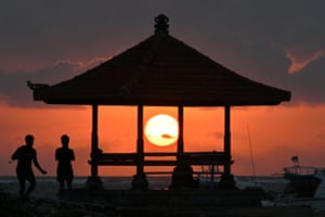 Anglers with fishing rods are silhouetted next to a pagoda as the sun rises above the horizon