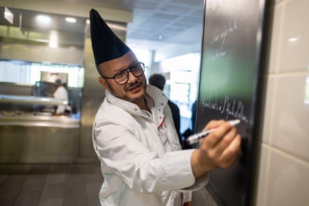 Farid Rouba writes on a blackboard while wearing chef whites