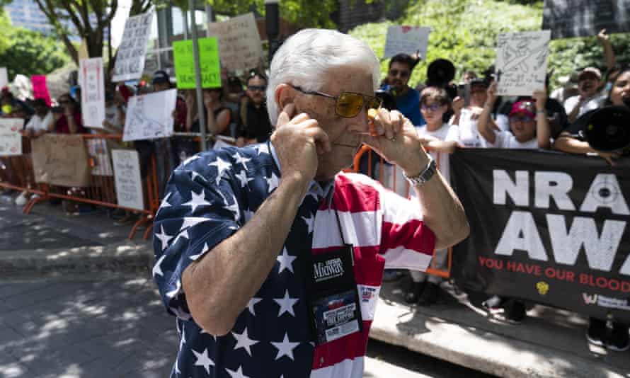 A man plugs his ears with his fingers as he walks past protesters during the NRA's annual meeting.