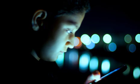 Young boy looking at cellphone in darkness.