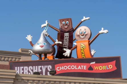 Mascots dressed like chocolate candy smile and wave in front of a sign for Hershey’s Chocolate World